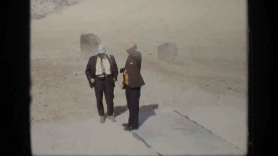 Two men in suits stand at a cleared outdoor site in Moscow, 1971, one with equipment near his chest and the other turned toward him.