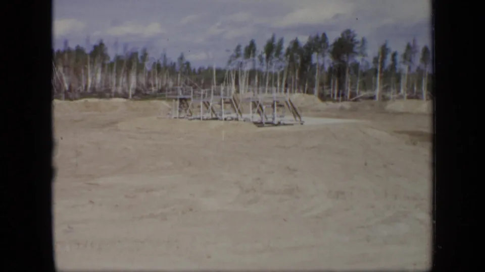 A wide 1971 Moscow site view shows cleared sandy ground, low wooden scaffolding or framing, and a forested background under a cloudy sky.