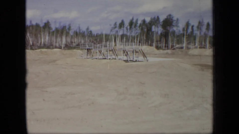 1971 Moscow industrial-site view with sandy ground, a low metal platform, railings, and birch trees in the background.