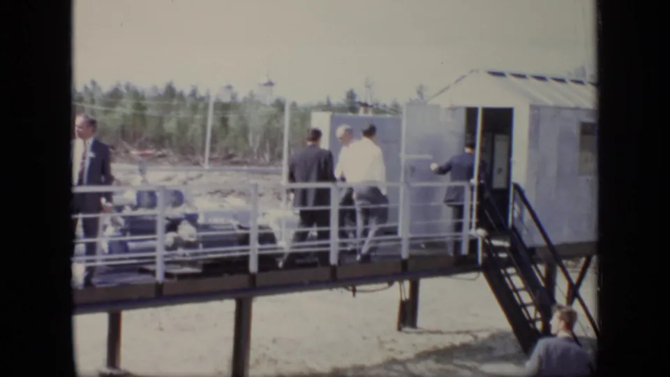 1971 Moscow footage showing suited men on a raised industrial walkway near a small structure, stairs, railings, and sandy ground.