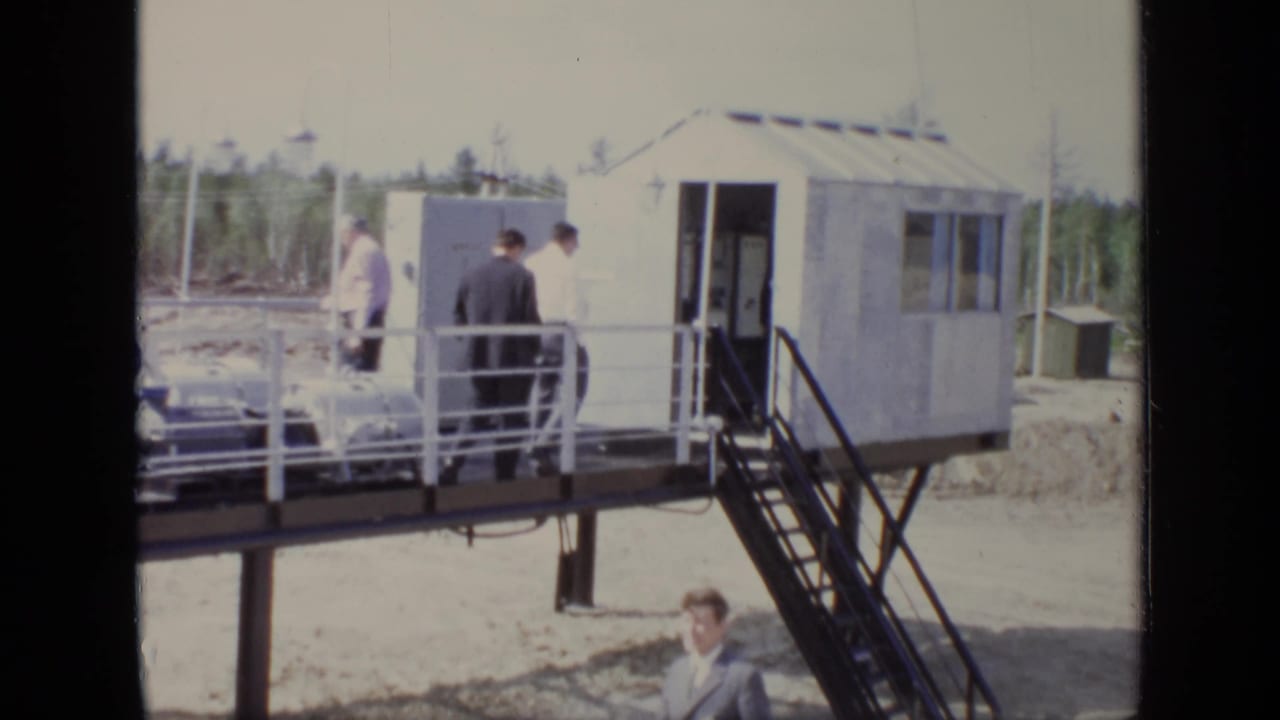 Men walk along the raised platform near stairs and a small metal-sided building.
