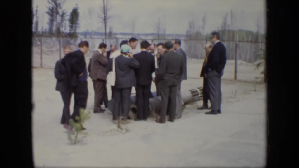 1971 Moscow footage shows men in formal clothing clustered around industrial equipment with fencing and trees behind them.
