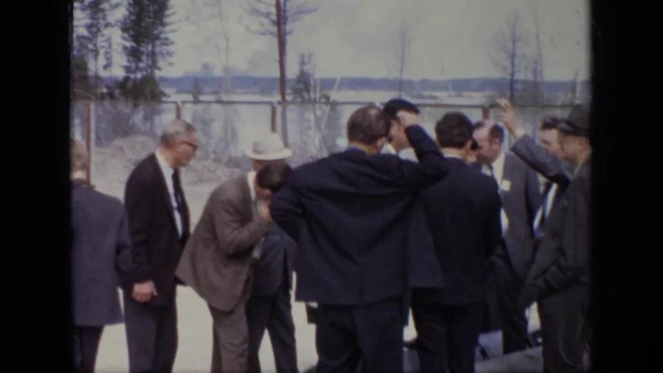 Closer 1971 Moscow view of several suited men in conversation beside a pipe or machinery component at an industrial site.