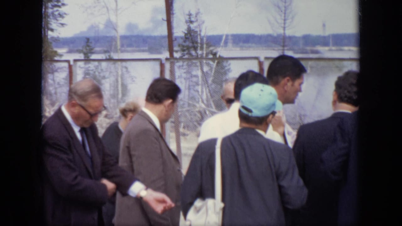 In 1971 Moscow footage, several adult men stand near fencing as one man appears to check his wristwatch.