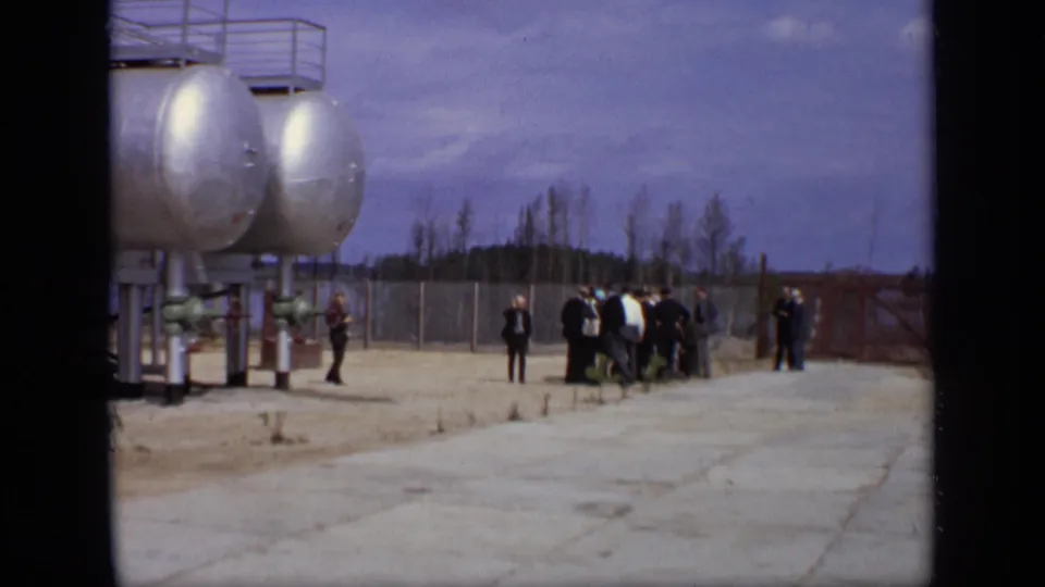 Suited men appear to pause near silver tanker tanks at a Moscow industrial site filmed on 8mm in 1971.