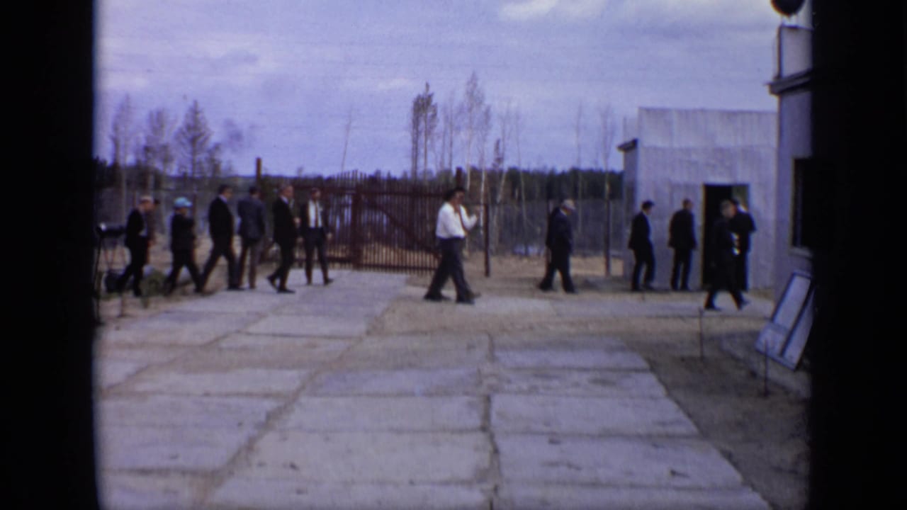 1971 Moscow 8mm frame showing men in dark suits crossing a concrete courtyard beside a small building and tall fence.