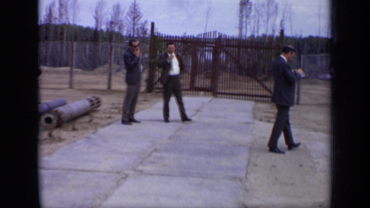 1971 Moscow 8mm frame with two suited men near a metal gate as another man walks along the concrete path.