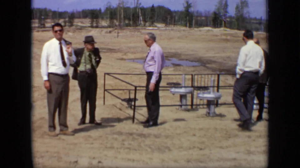 A small group of adult men in formal clothing stands near metal railings and exposed pipes at the Moscow site.