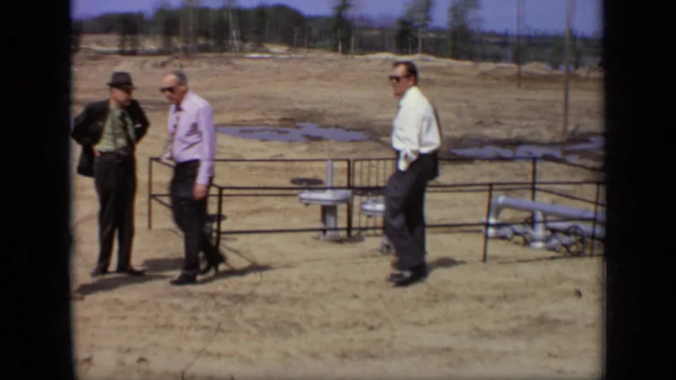 Three adult men, including one in a hat and one in sunglasses, converse beside railings and pipes in Moscow in 1971.