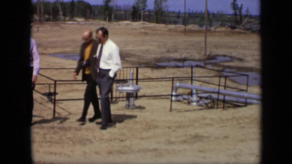 Two adult men in formal clothing walk past metal railings and exposed pipes at the Moscow outdoor site.