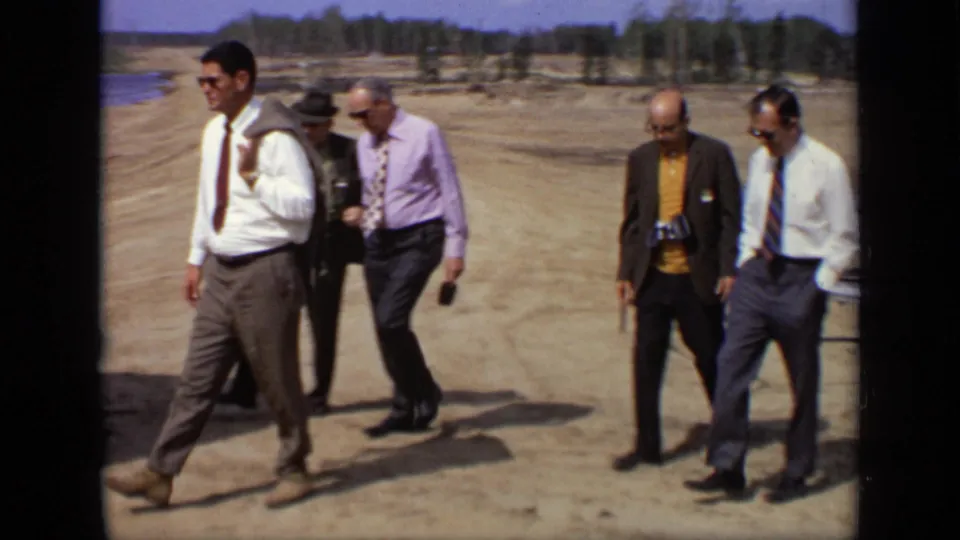 Five adult men, several in shirts and ties and one carrying a camera, cross a dusty Moscow site in the 1971 8mm footage.
