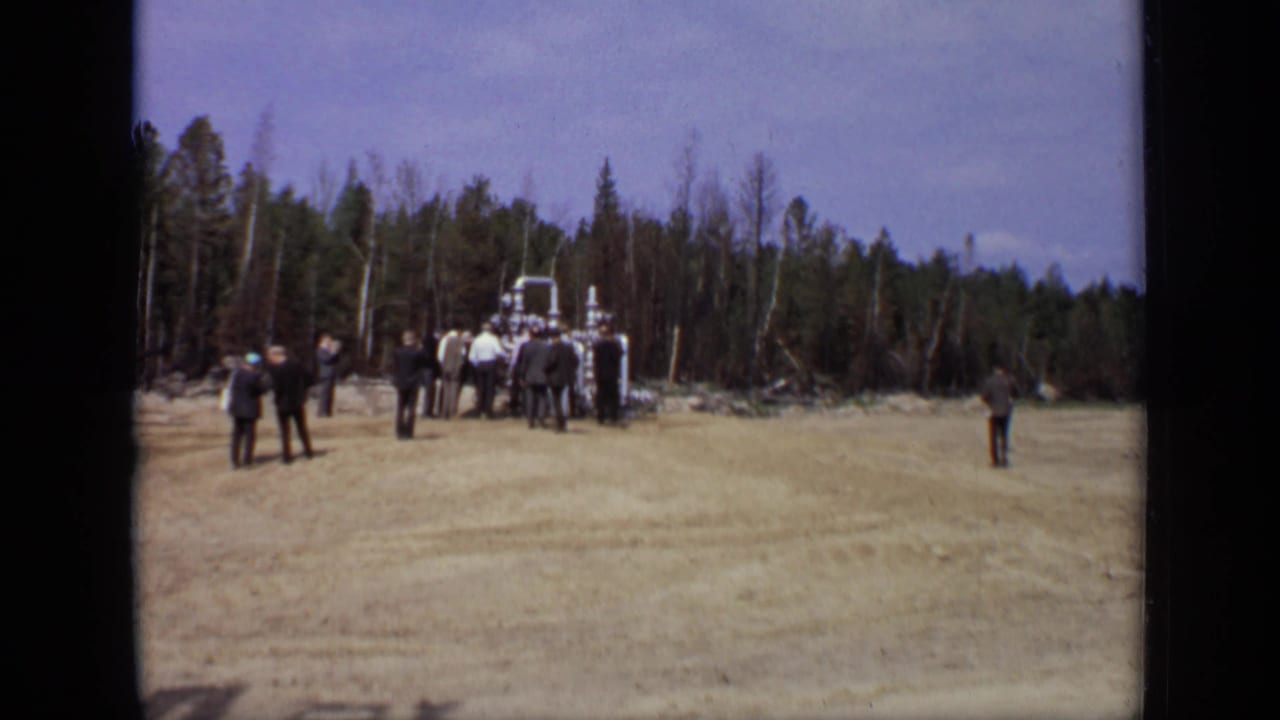 Men gather around industrial piping in a wooded field.