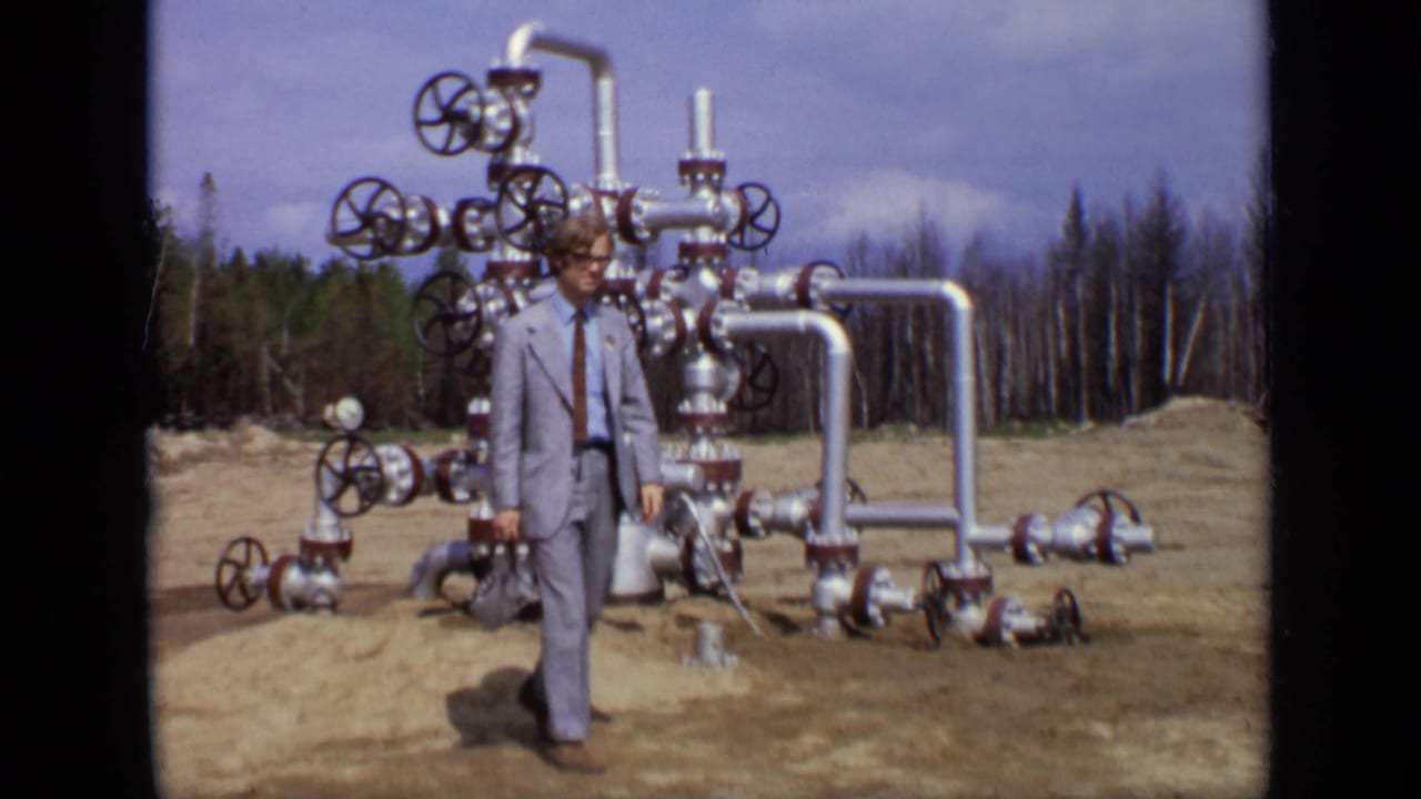 1971 Moscow frame with a suited man walking past a complex silver valve assembly in an outdoor clearing.