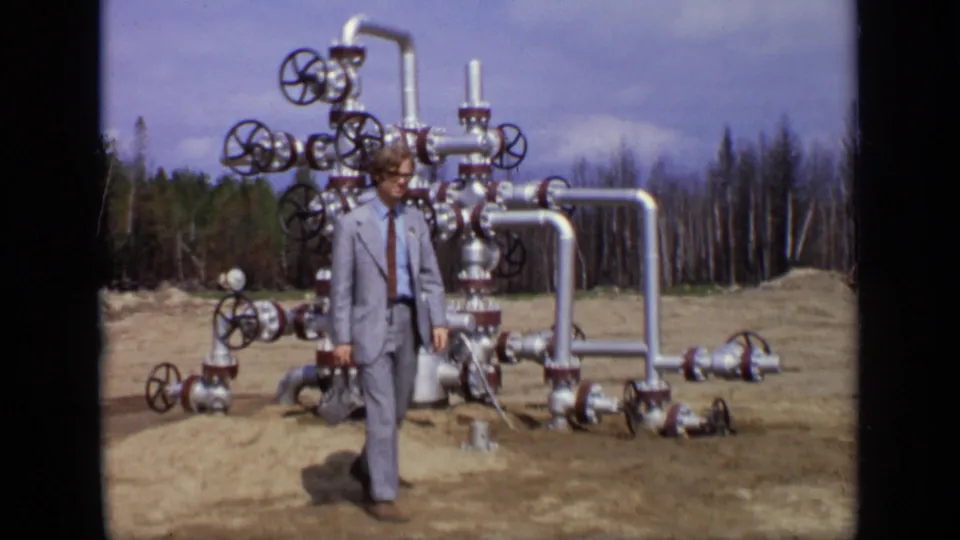 1971 Moscow frame with a suited man walking past a complex silver valve assembly in an outdoor clearing.