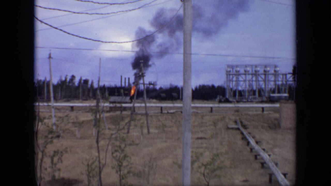 1971 Moscow-area 8mm frame showing a small fire with black smoke near utility poles, wires, and a distant industrial structure.