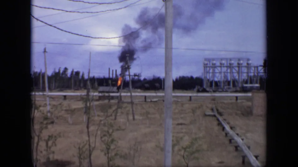 1971 Moscow-area 8mm frame showing a small fire with black smoke near utility poles, wires, and a distant industrial structure.