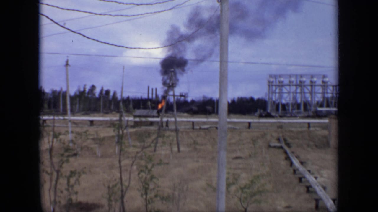 1971 Moscow-area home-movie view of flame and smoke in an open field framed by poles, wires, and industrial equipment.