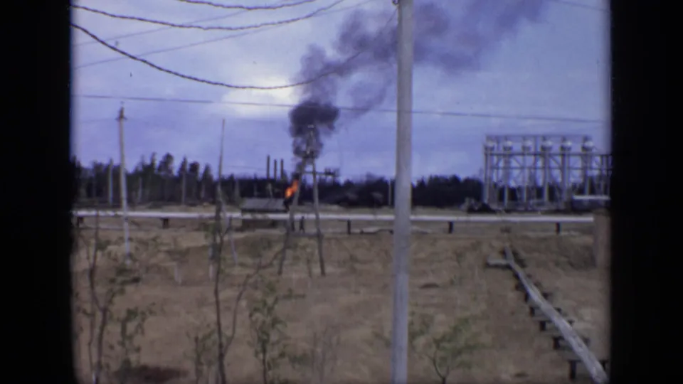 1971 Moscow-area home-movie view of flame and smoke in an open field framed by poles, wires, and industrial equipment.
