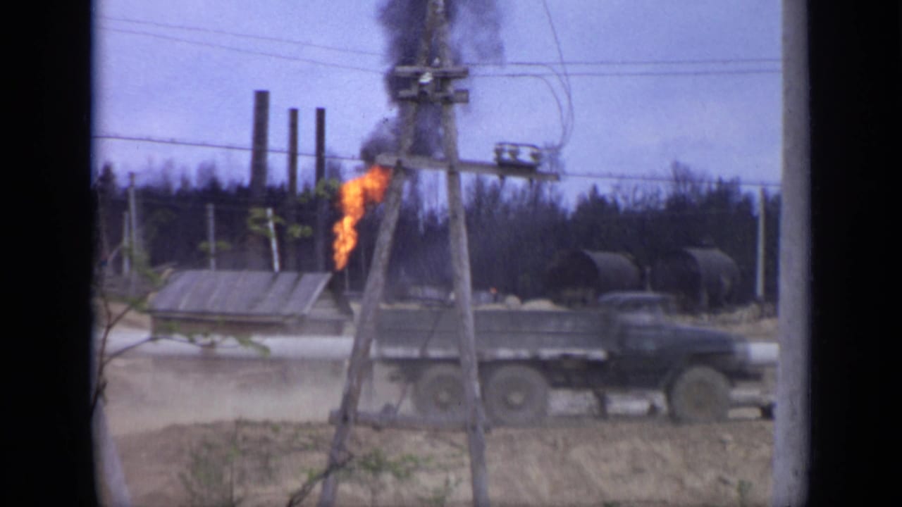 A dark truck passes the flaming grey structure at a Moscow industrial site, with overhead wires and black smoke visible behind it.