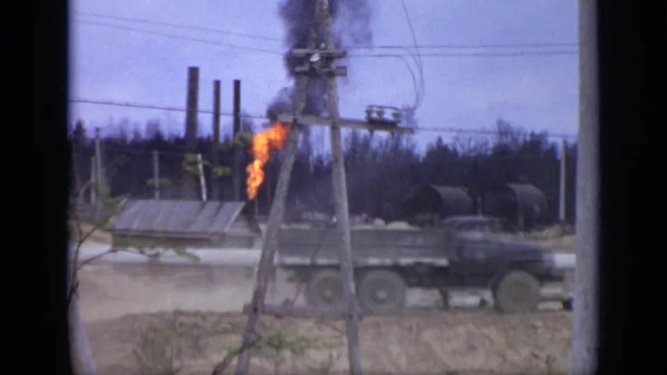 A dark truck passes the flaming grey structure at a Moscow industrial site, with overhead wires and black smoke visible behind it.