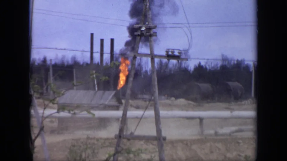 The truck has mostly left the frame while the orange flame and dark smoke remain near a small industrial structure in 1971 Moscow.