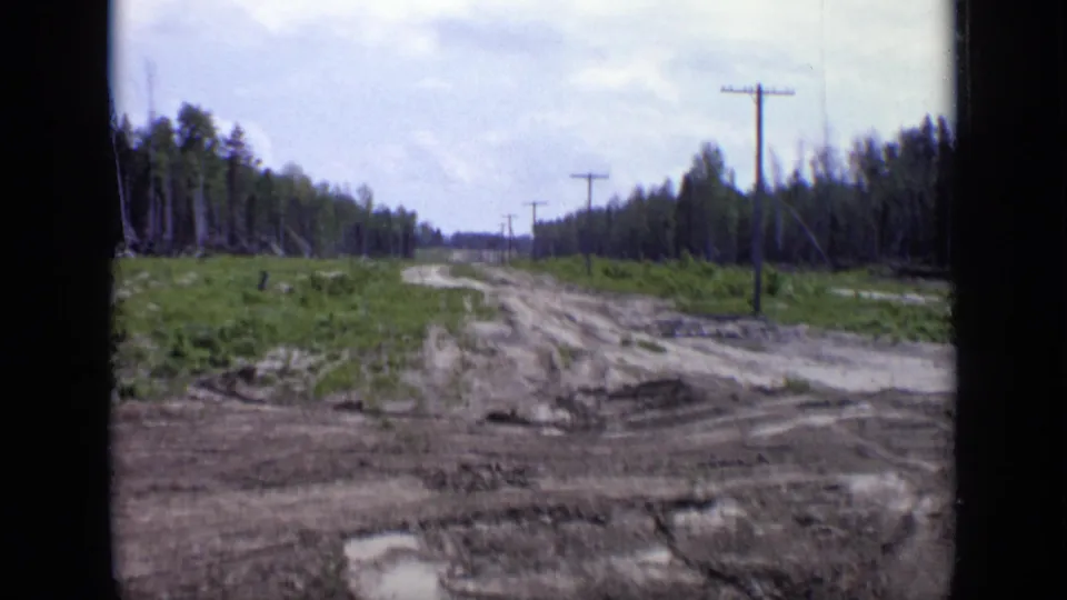 1971 Moscow frame showing muddy cleared land, a rough road, utility poles, and forest on both sides.