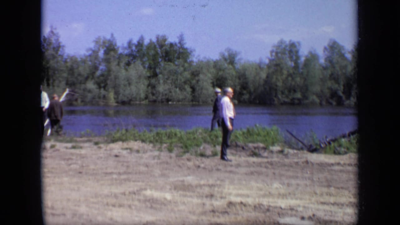 1971 Moscow riverbank view with one man standing in the foreground and several men walking near the water.
