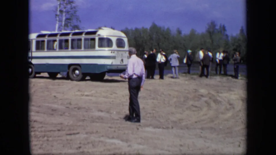 The lakeside scene widens to show a lone man in the foreground, a parked bus, and several people near the water.