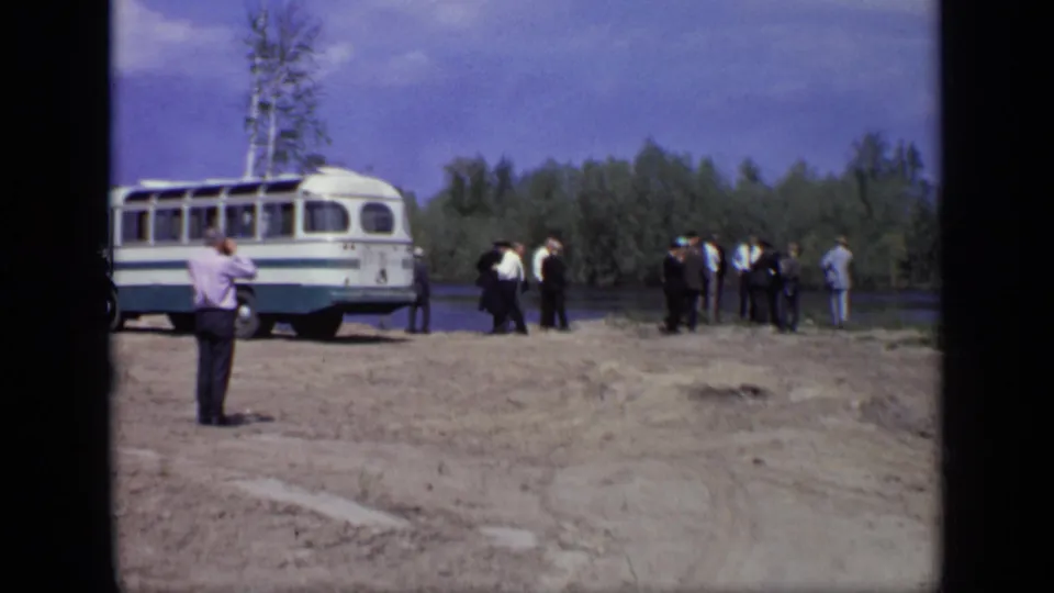 The 1971 Moscow clip shows men clustered near a white bus on a dirt clearing with river and wooded background visible.