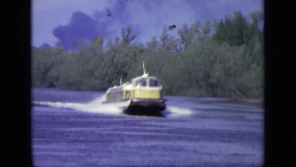 The yellow speedboat continues along the Moscow river, framed by trees, blue sky, smoke in the distance, and visible 8mm film marks.