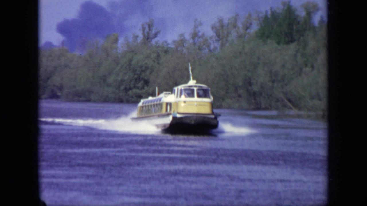 1971 Moscow home-movie frame showing a yellow hydrofoil crossing water with a white wake and tree-lined shoreline.