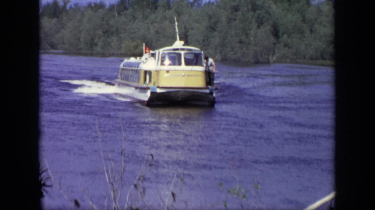 Yellow-and-white passenger boat moves along a broad river near wooded banks.