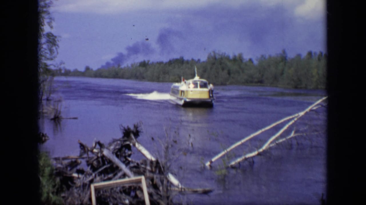 1971 Moscow river view with the yellow passenger boat moving away, shoreline debris at right, and a smoke plume in the distance.