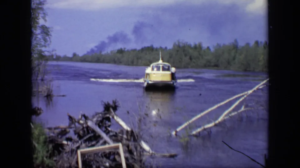 1971 Moscow river scene with the yellow-and-white boat receding, foreground branches, wooded banks, and smoke visible in the distance.