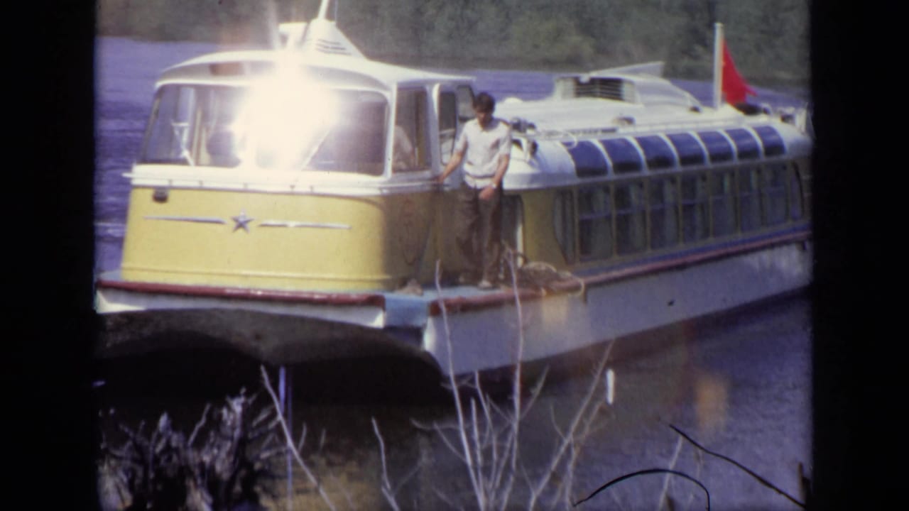 1971 Moscow frame with a man standing on the bow area of a yellow and white hovercraft marked by a star emblem and red flag.