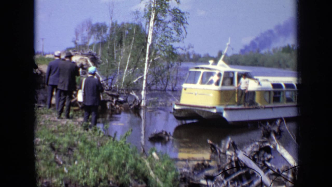 Yellow-and-white passenger boat at a muddy riverbank with suited people nearby.