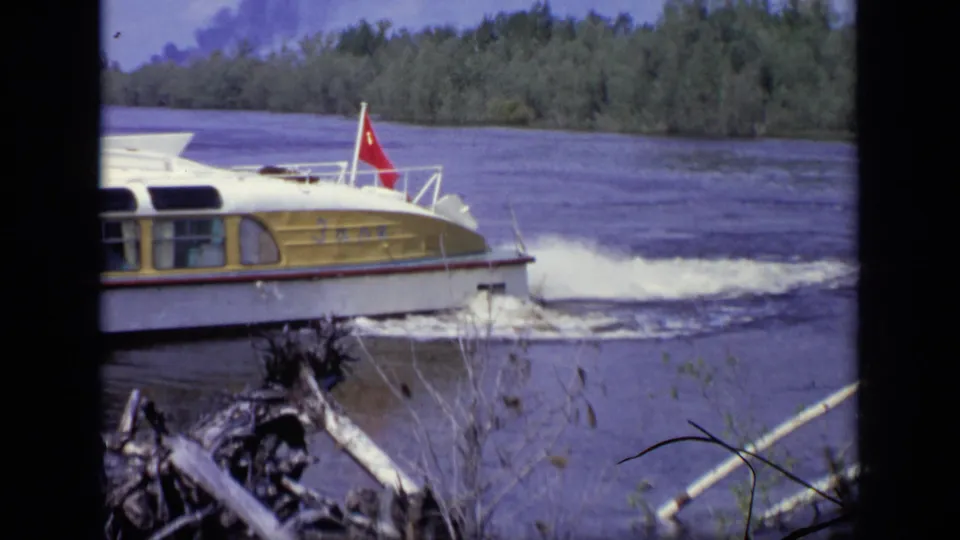 The yellow and white ferry continues along the river, its red flag visible against the wooded Moscow shoreline.