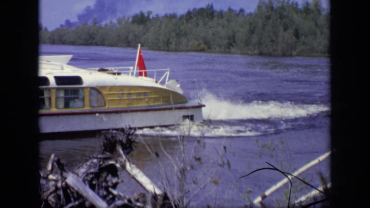 Yellow and white motorboat moving across a river with trees in the background.