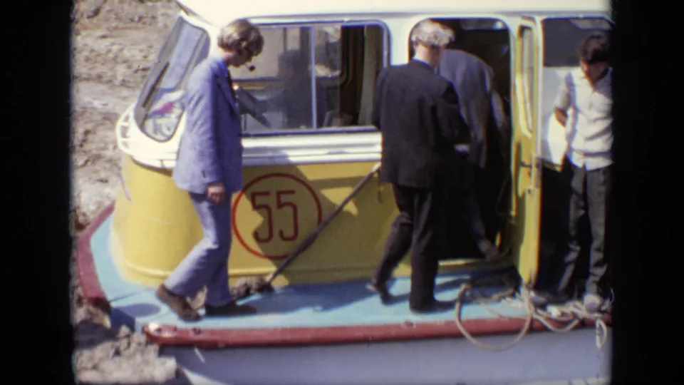 Men in suits enter the open doorway of the yellow and blue boat marked 55, with another person standing near the right edge.