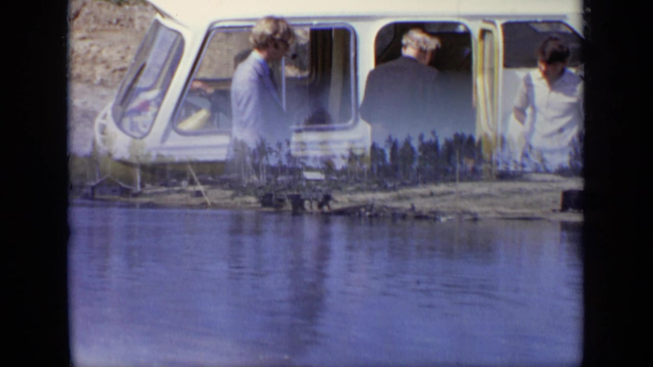 Adults stand beside a yellow boat at a waterfront dock.