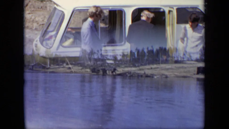 1971 Moscow home-movie frame showing adults boarding or standing near a yellow water taxi at the shore.