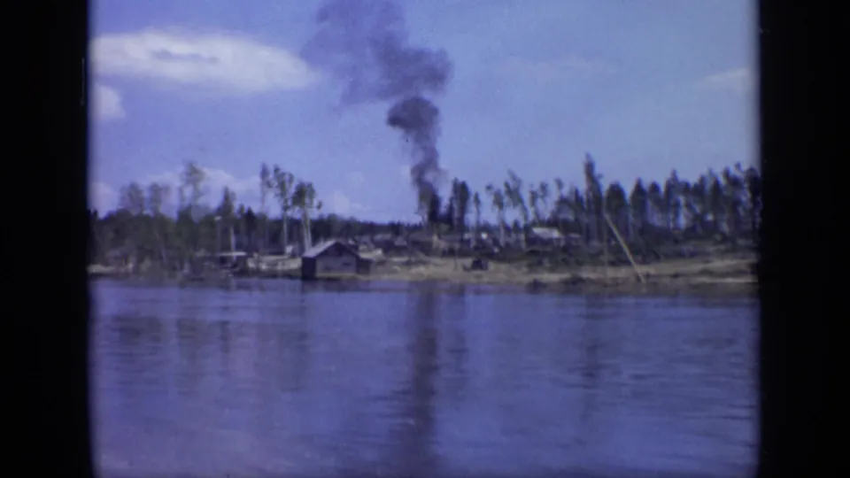 1971 Moscow riverbank scene with a low building, wooded shore, and smoke rising from an unseen source inland.