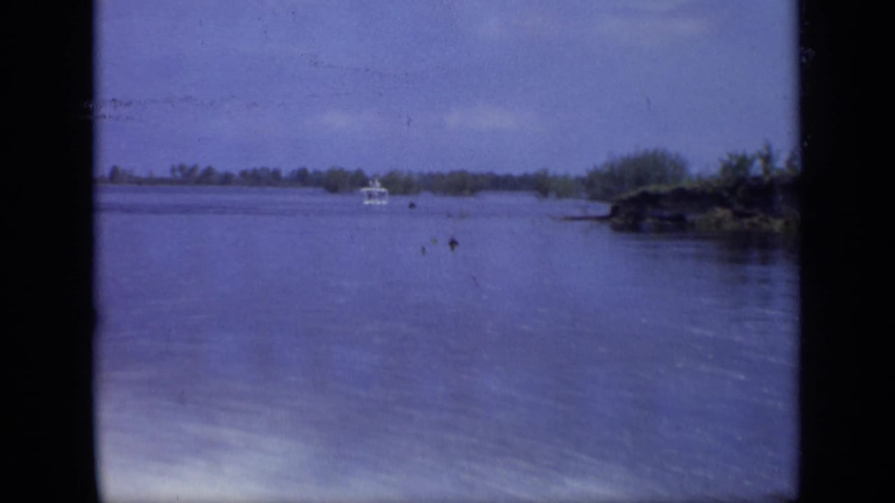 Small white boat in the distance on broad floodwater with low shoreline vegetation.