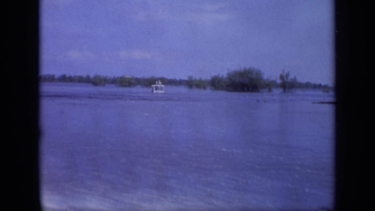 1971 8mm Moscow frame with a small white boat on wide blue floodwater and partially submerged vegetation in the distance.