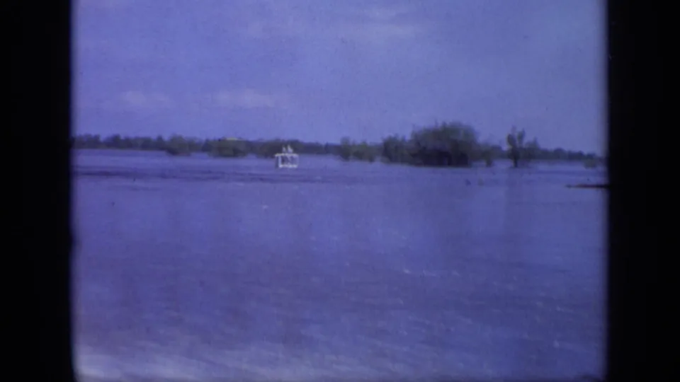 1971 8mm Moscow frame with a small white boat on wide blue floodwater and partially submerged vegetation in the distance.