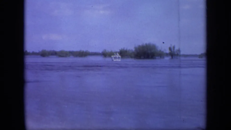 Home-movie view from 1971 Moscow showing floodwater, a distant small boat, and tree tops rising from the water.