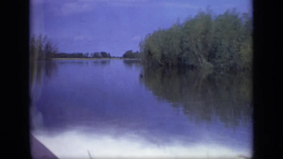1971 8mm wide view near Moscow showing a calm lake, reeds along the bank, distant trees, and blue-toned water reflections.
