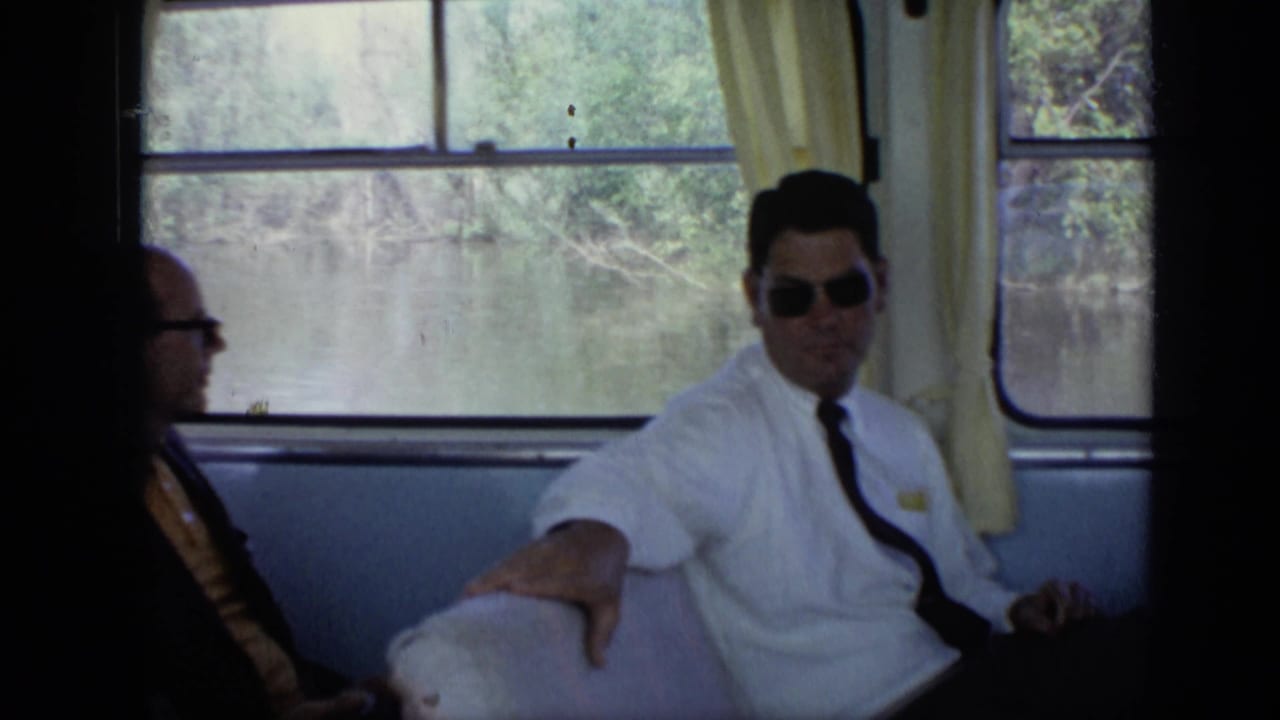 Men in suits seated inside a boat cabin beside wide river-facing windows.