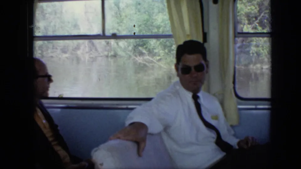 1971 Moscow boat cabin scene with suited men seated near windows, yellow curtains, and trees visible across the water.