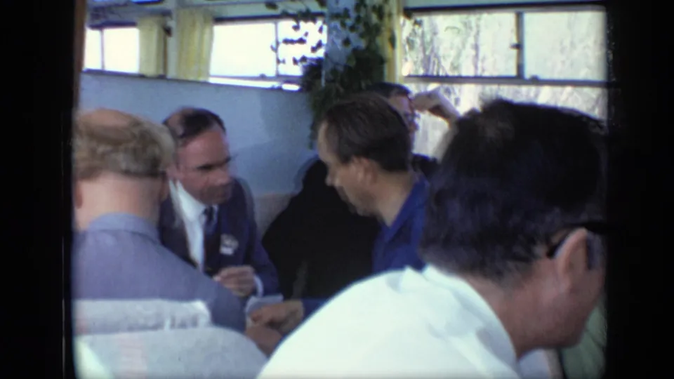 1971 Moscow train-compartment scene with adult men in suits and collared shirts talking under bright window light.